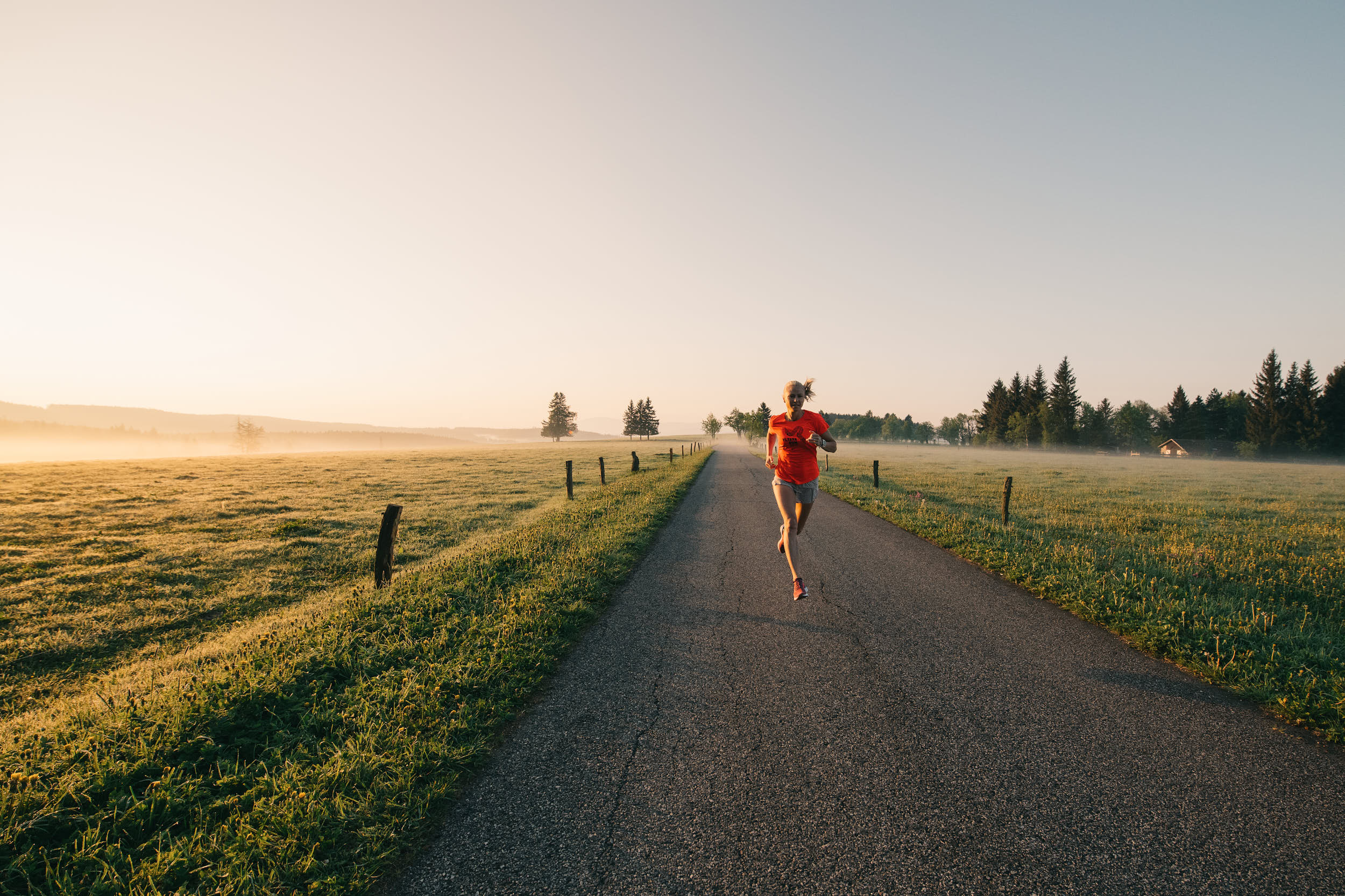 Running apparel campaign: woman running through beautiful landscape at dawn.