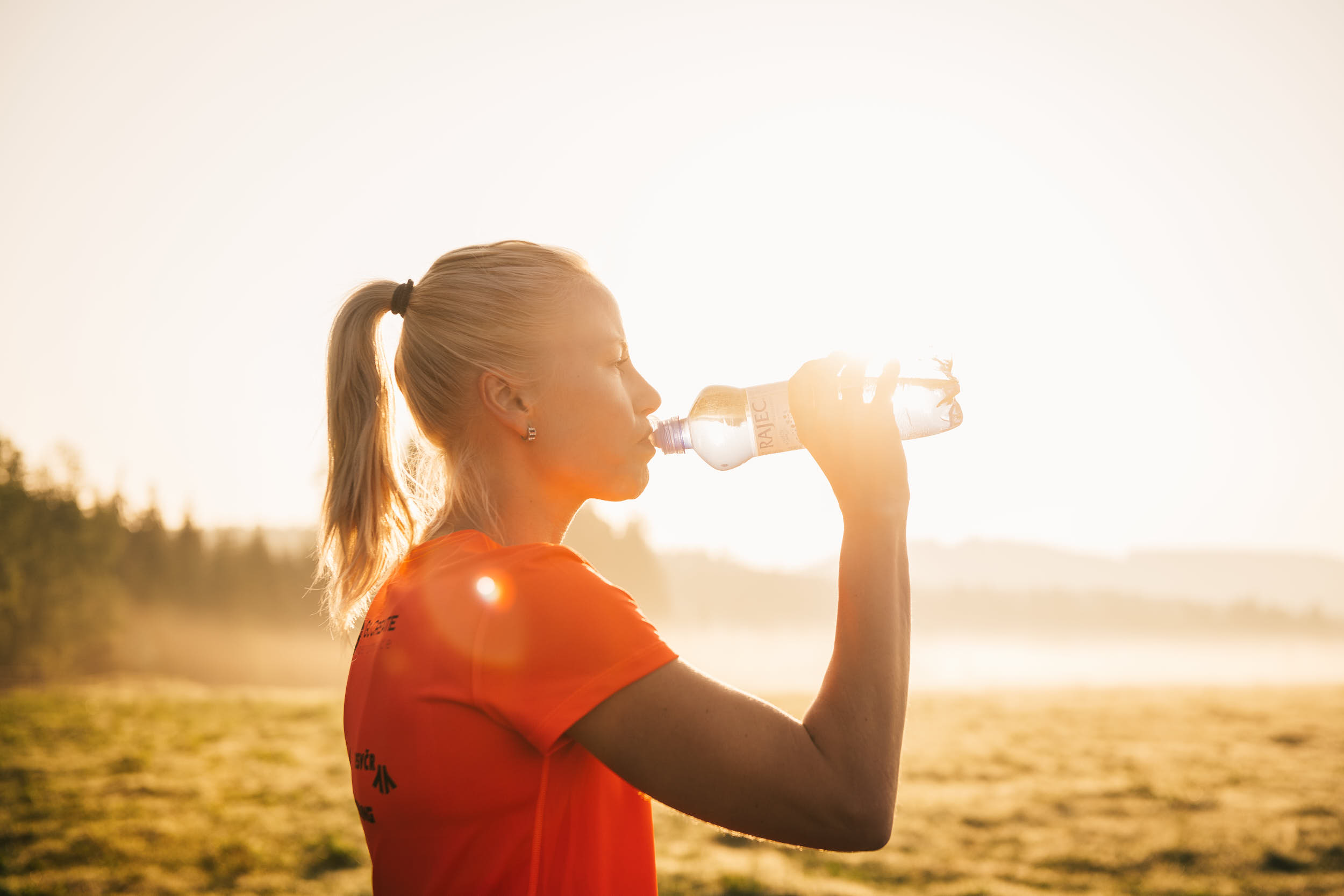 Female runner drinking water in a beautiful sunlit landscape.