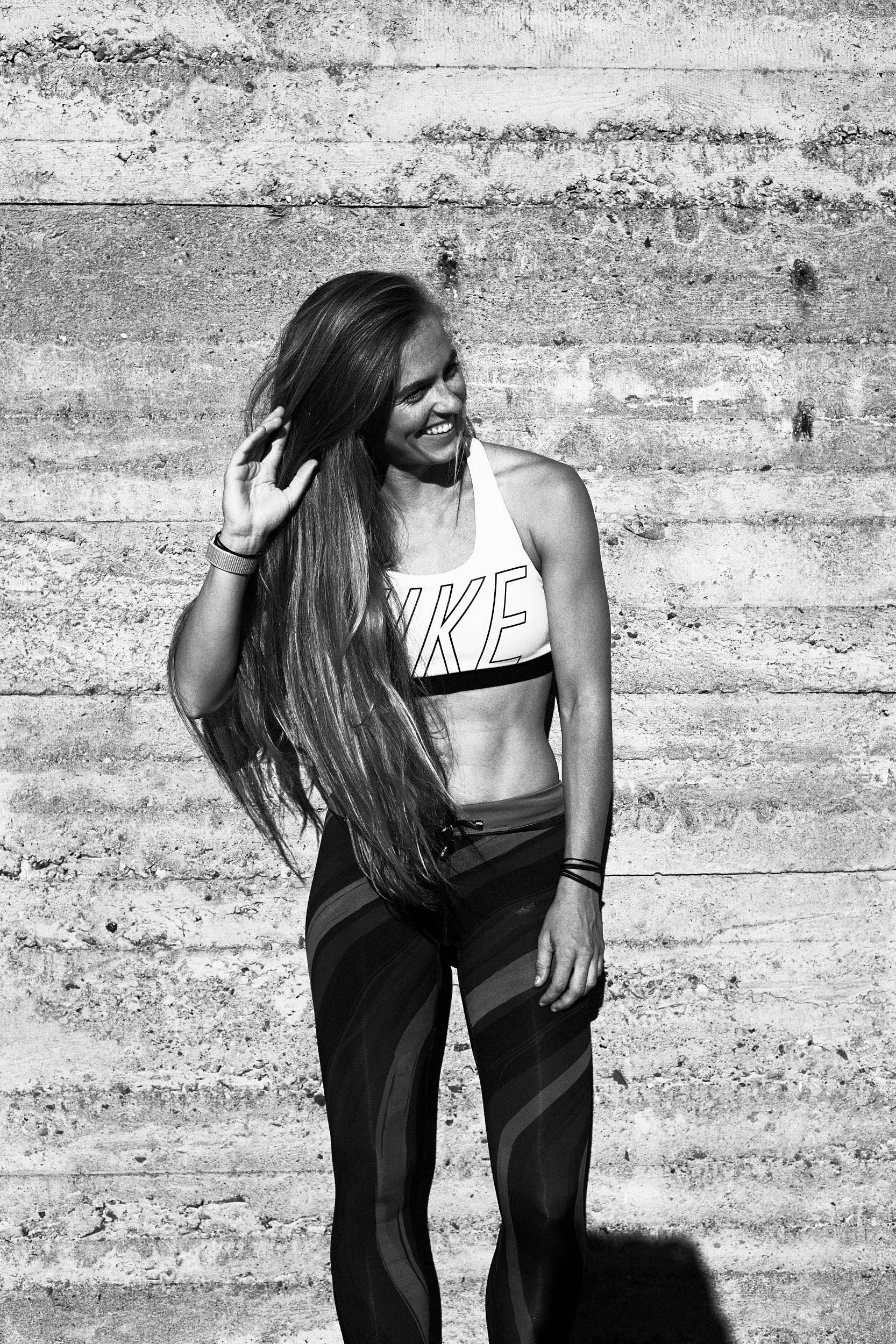 Black and white portrait of a female runner in front of a concrete wall with strong shadows.