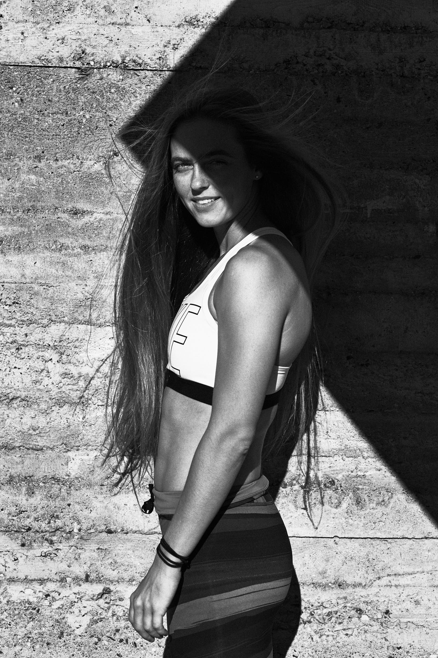 Black and white portrait of a female runner in front of a concrete wall with strong shadows.