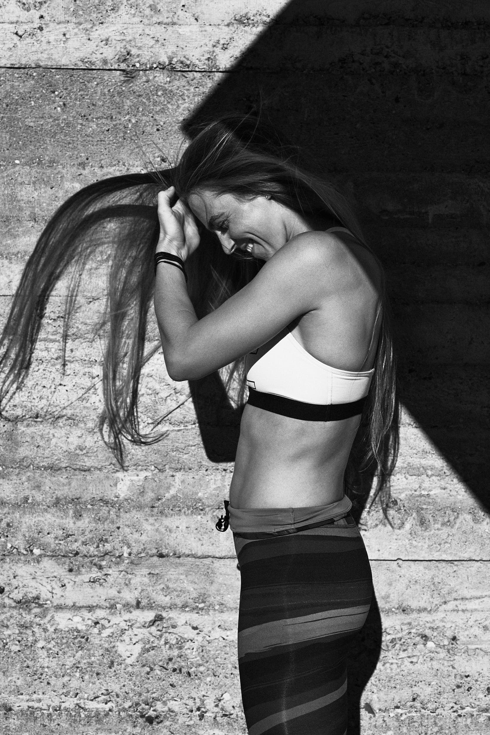 Black and white portrait of a female runner in front of a concrete wall with strong shadows.