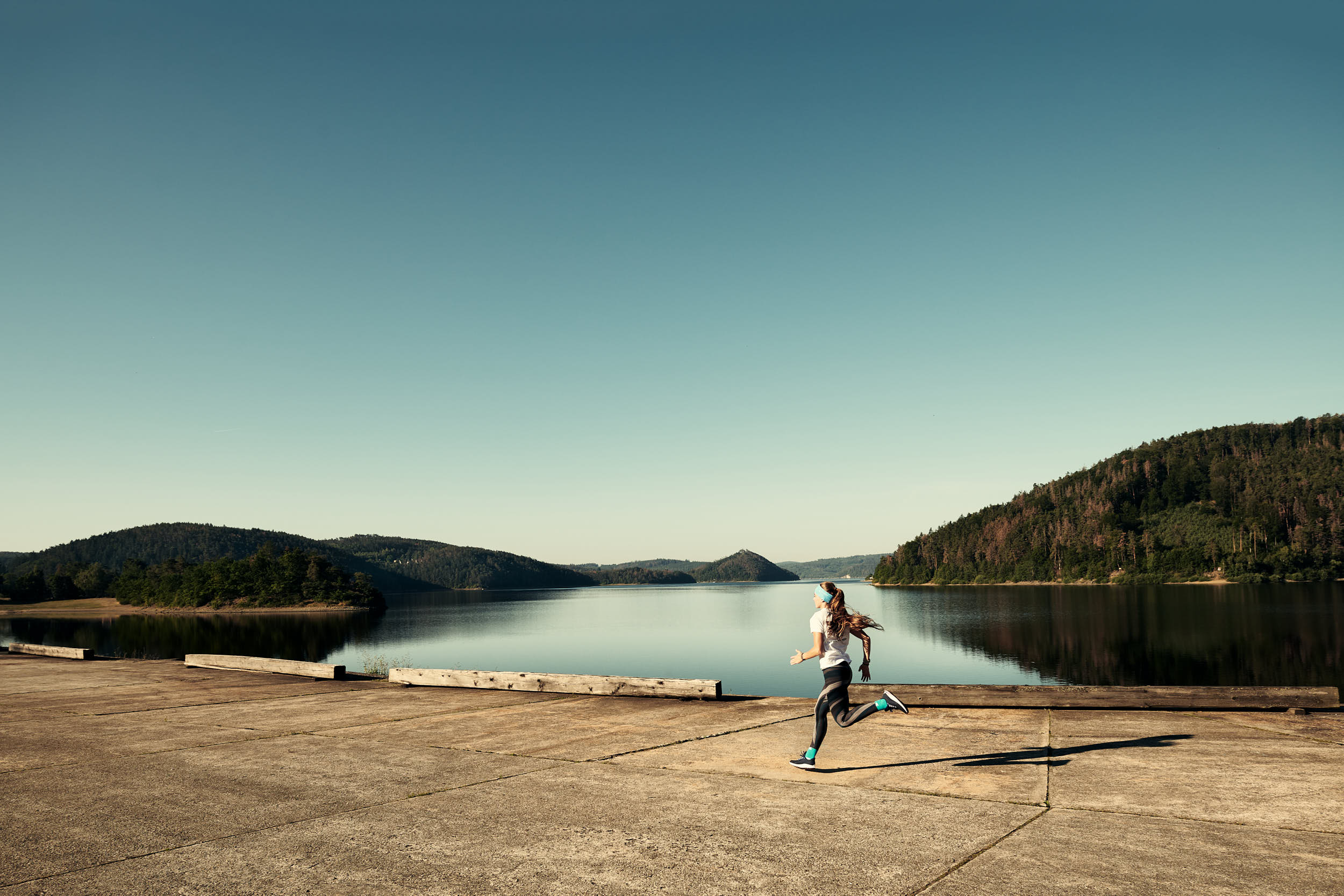 Girl running alongside a dam on a beautiful sunny day with clear sky.