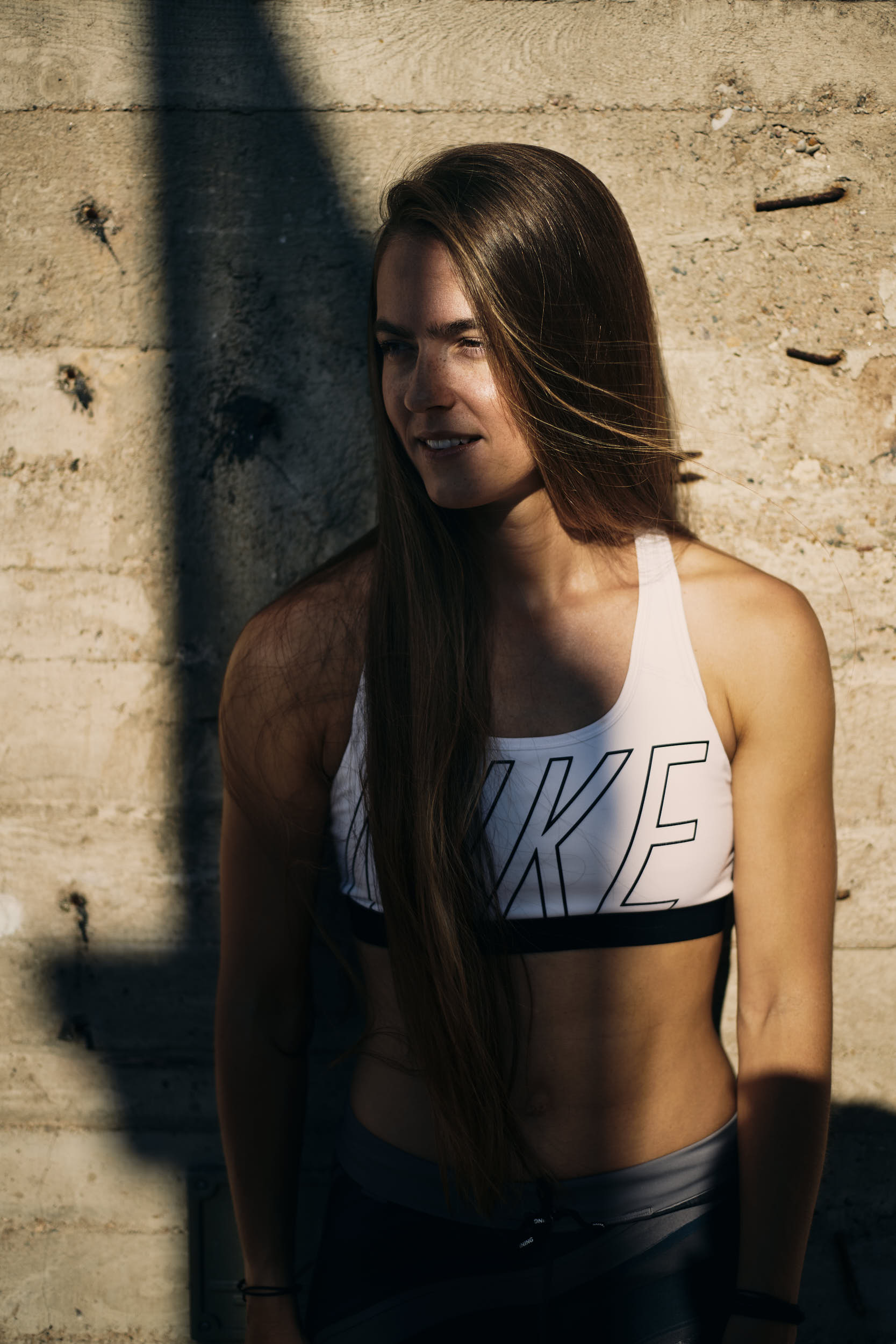 Active lifestyle photography: portrait of a girl posing in running apparel against a concrete wall.
