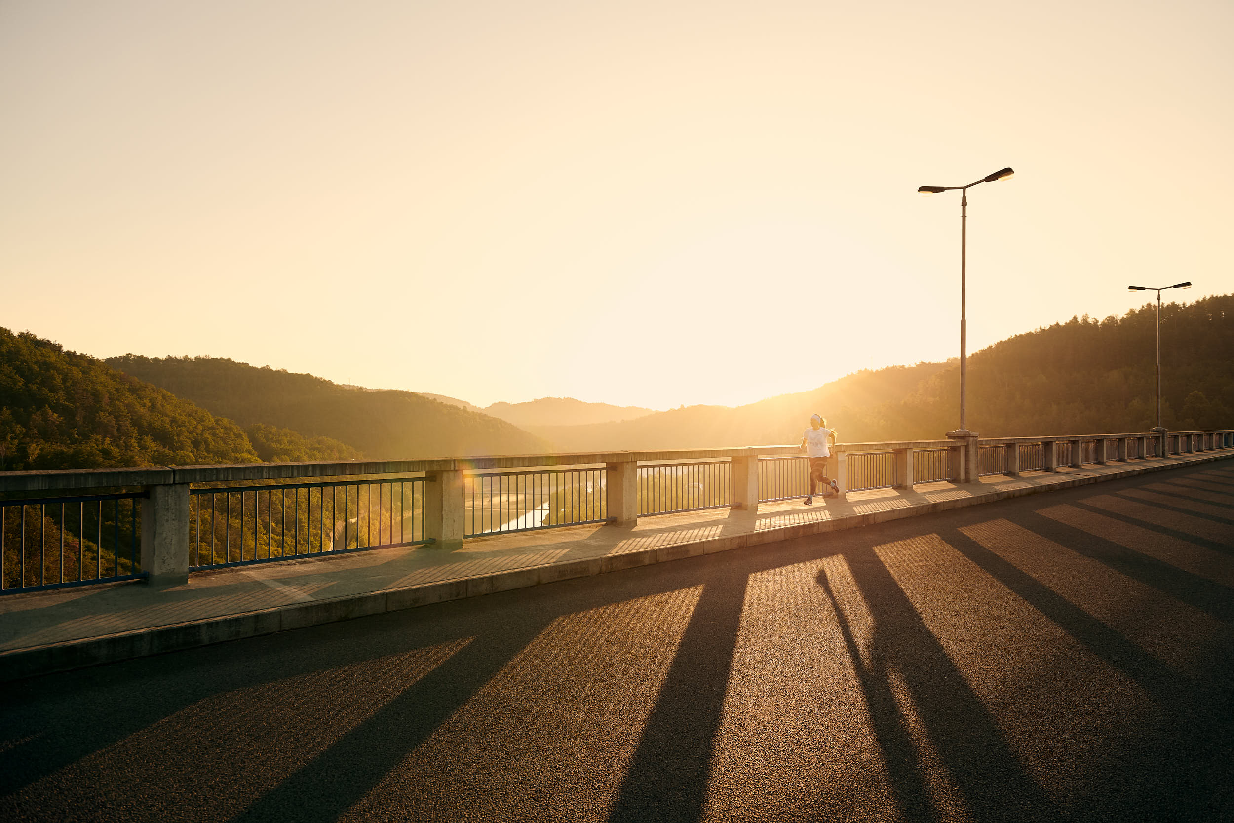 Sport advertising photography: girl running across a bridge in beautiful morning light.