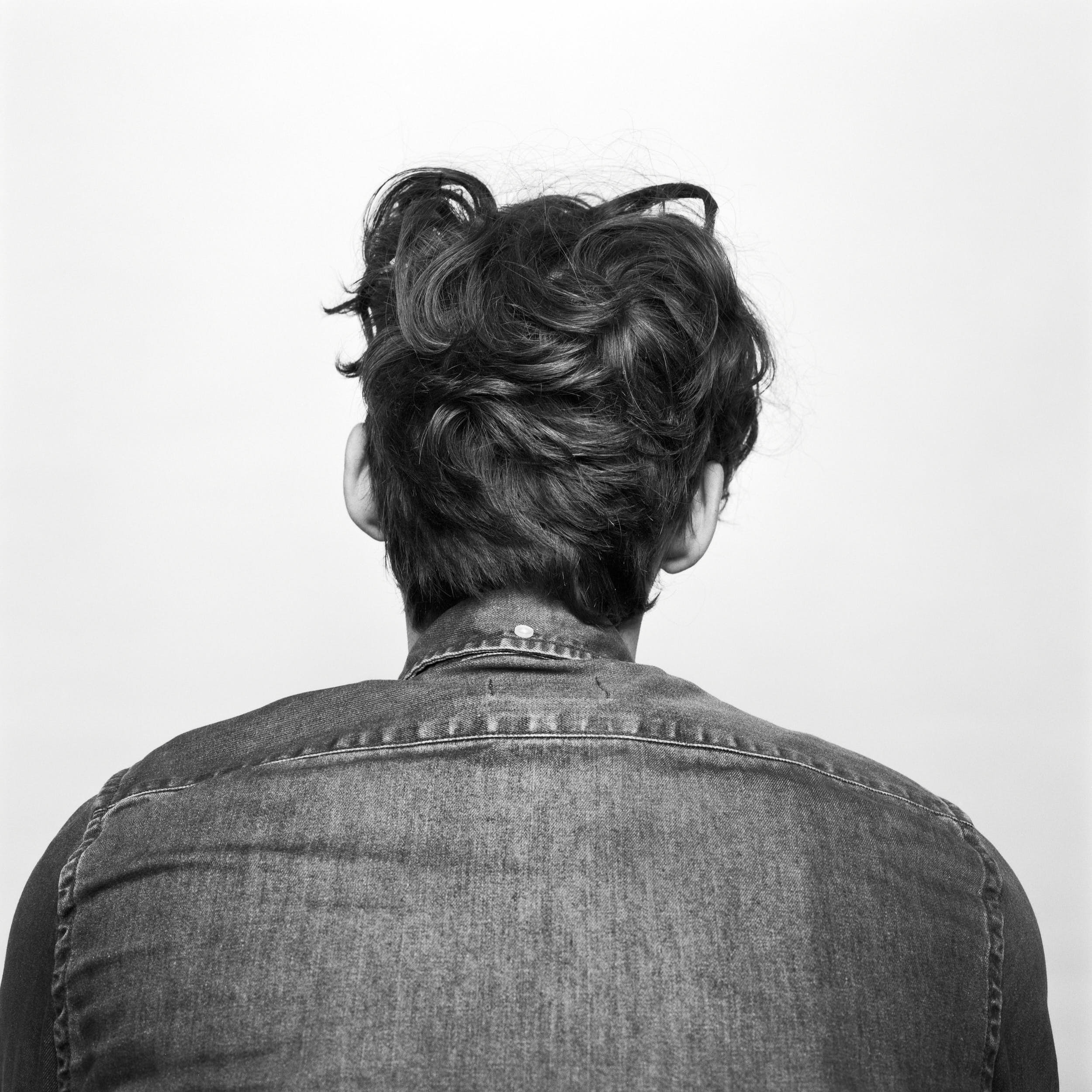 Studio portrait photography: man with curly hair and denim shirt turned away from the camera.