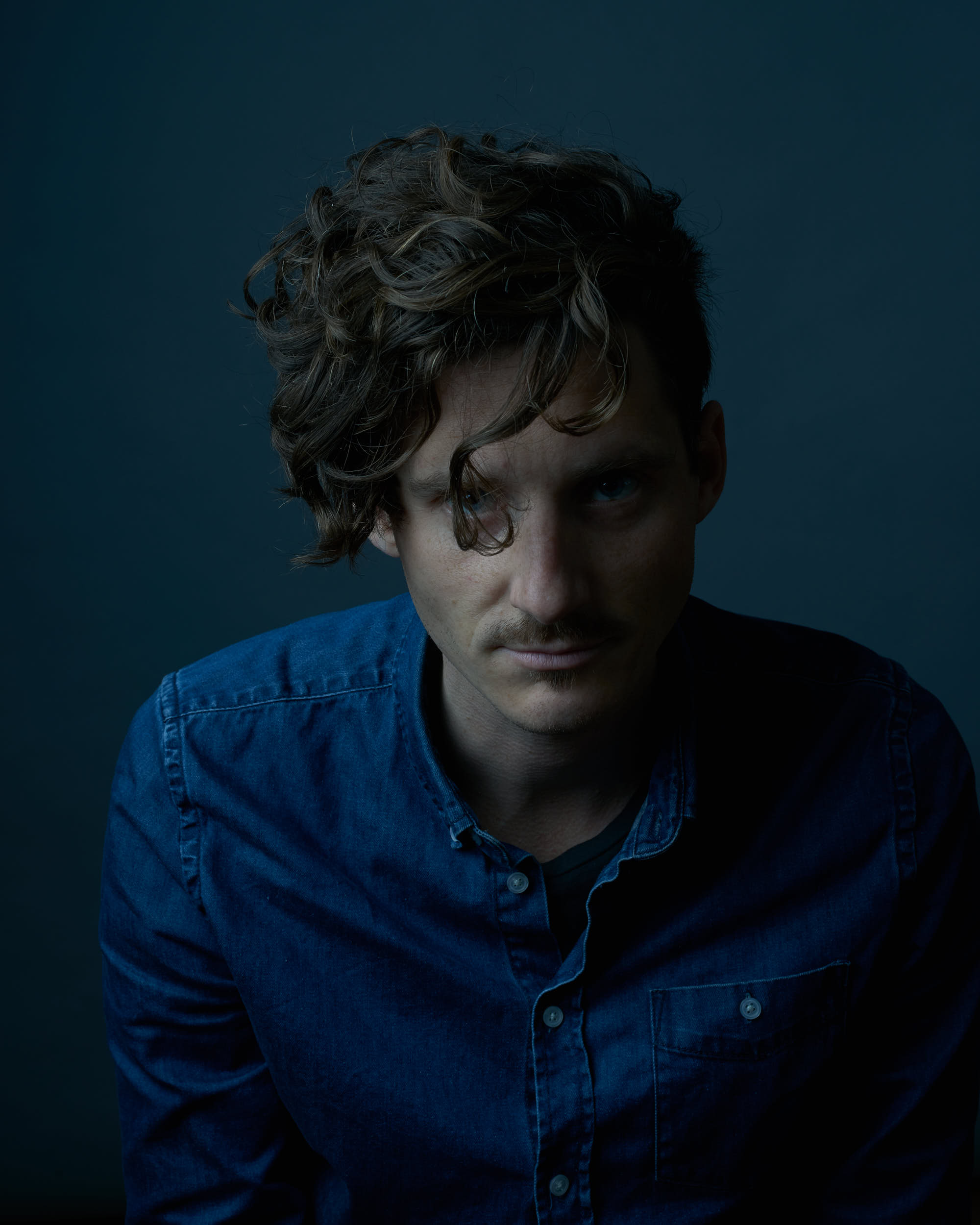 Man with original haircut in a dark cinematic studio portrait.