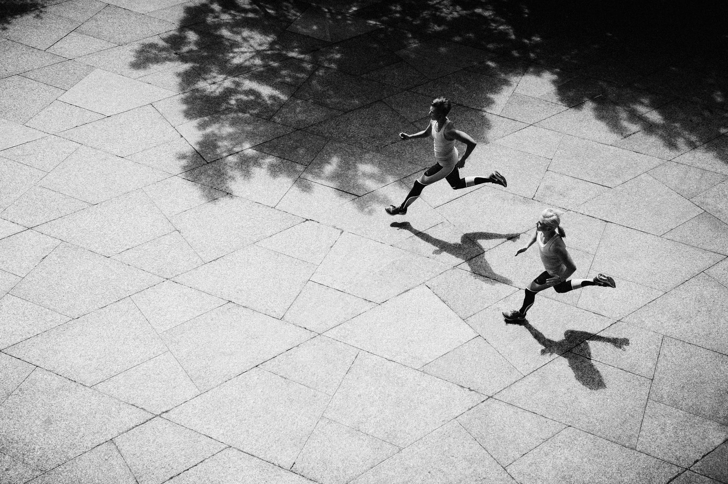 Black and white sport photography: two girls running on marble pavement shot from elevated perspective with strong contrast.