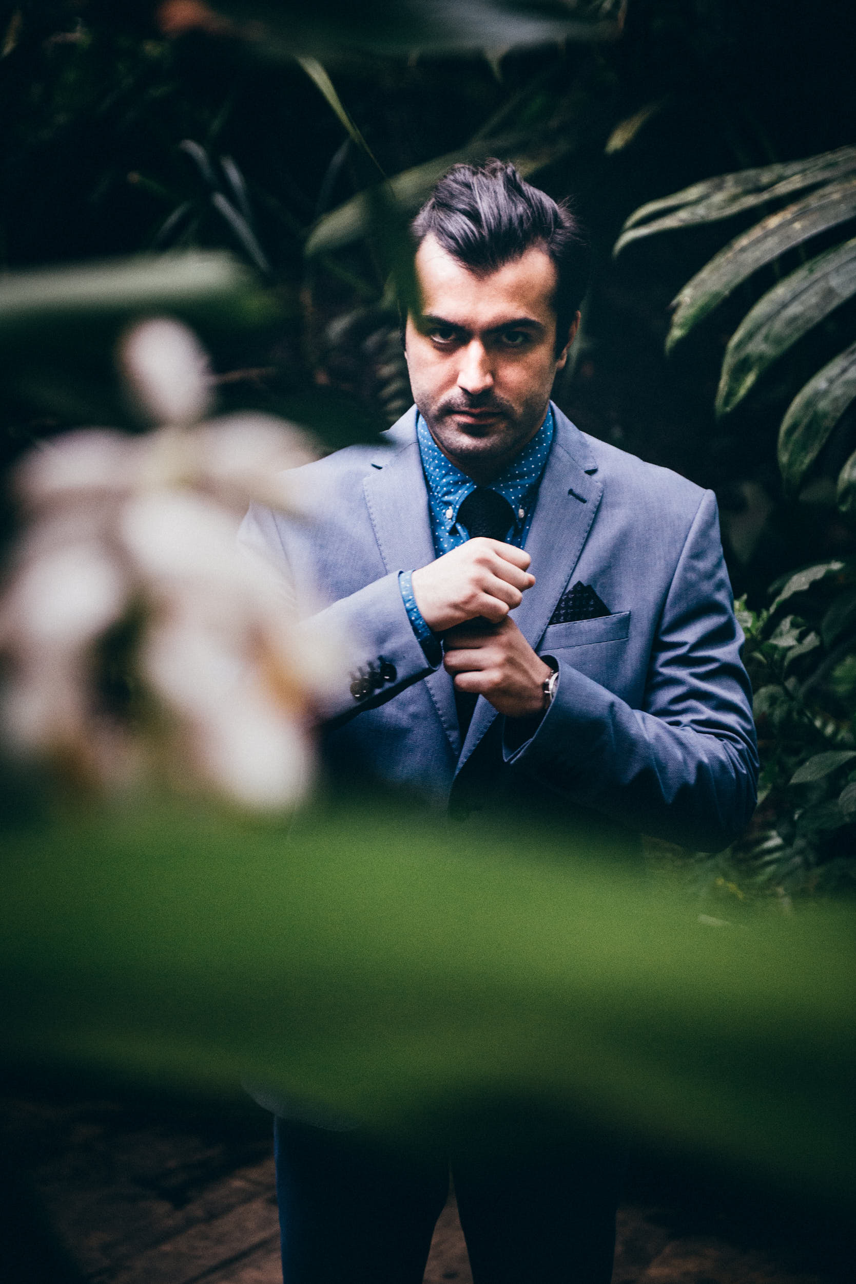 Man adjusting his suit surrounded with green plants.