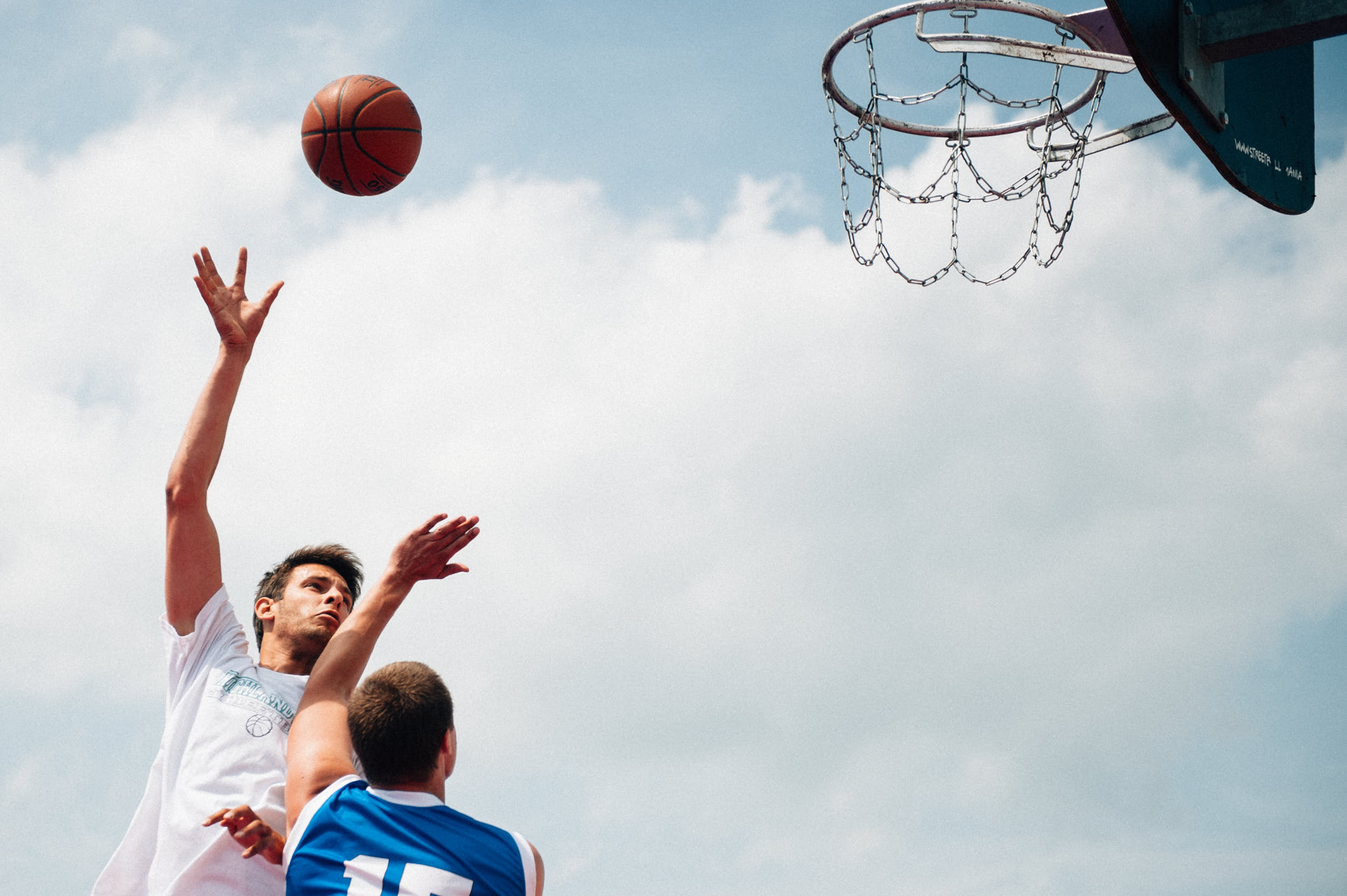 Basketball player shooting on a hoop at a court outdoors.