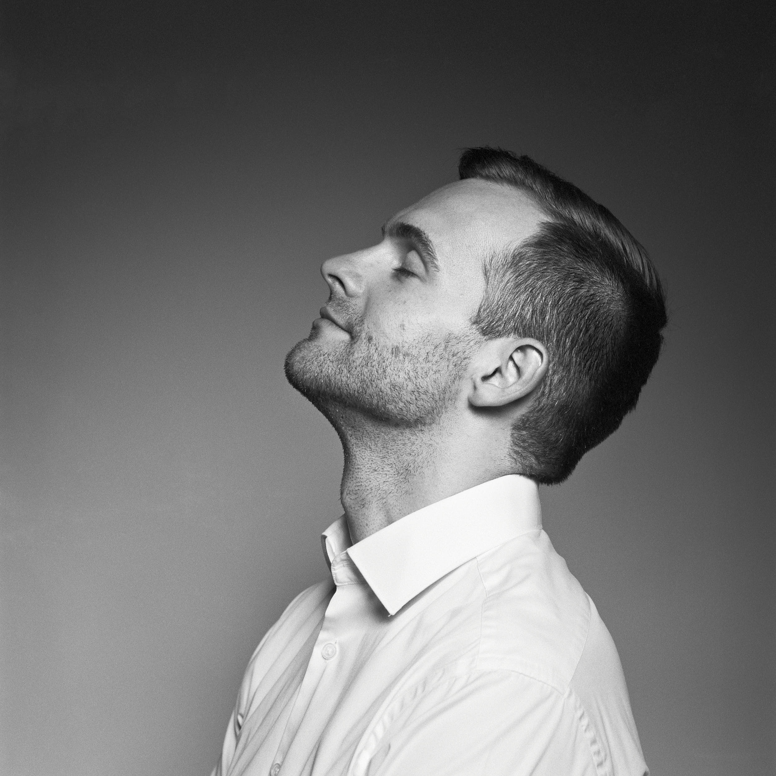 Black and white studio portrait of a man with closed eyes shot from the side.