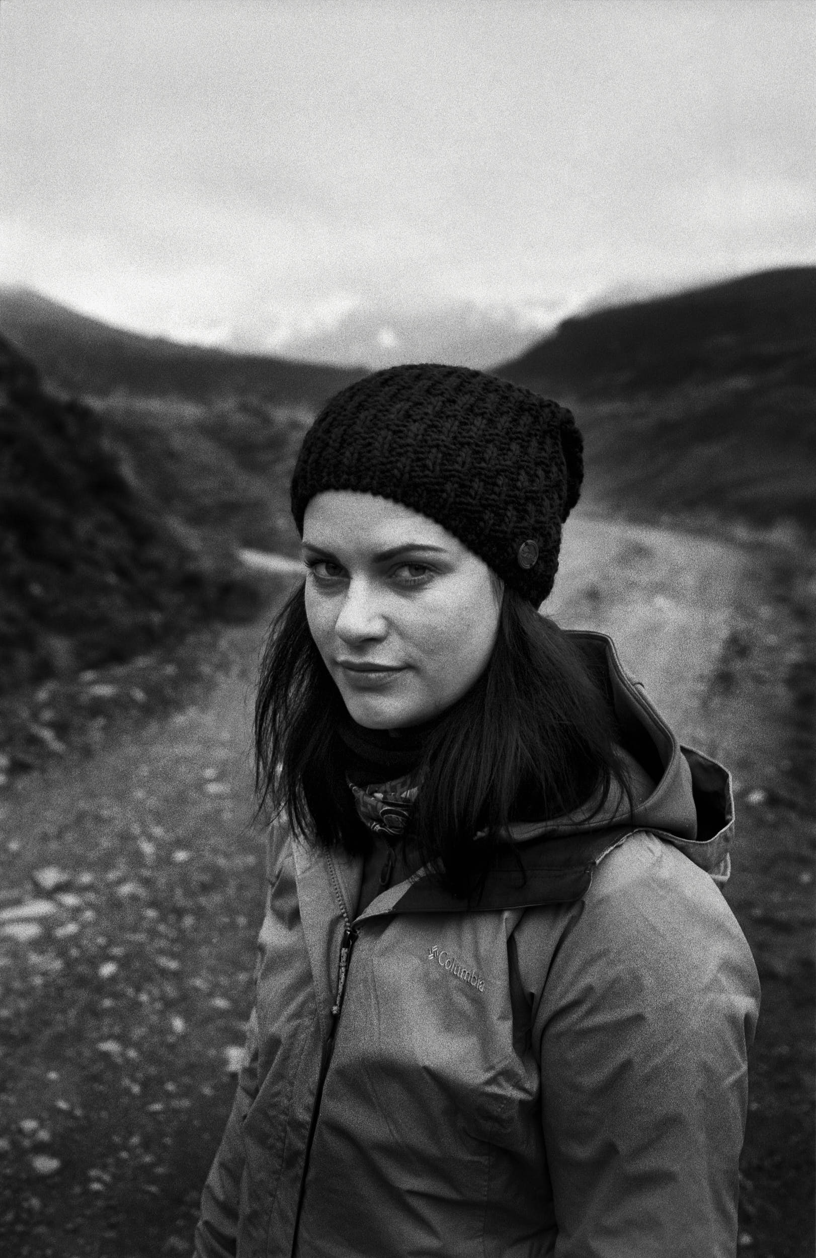 Woman on a mountain path dressed in outdoor apparel in a classic black and white film portrait.