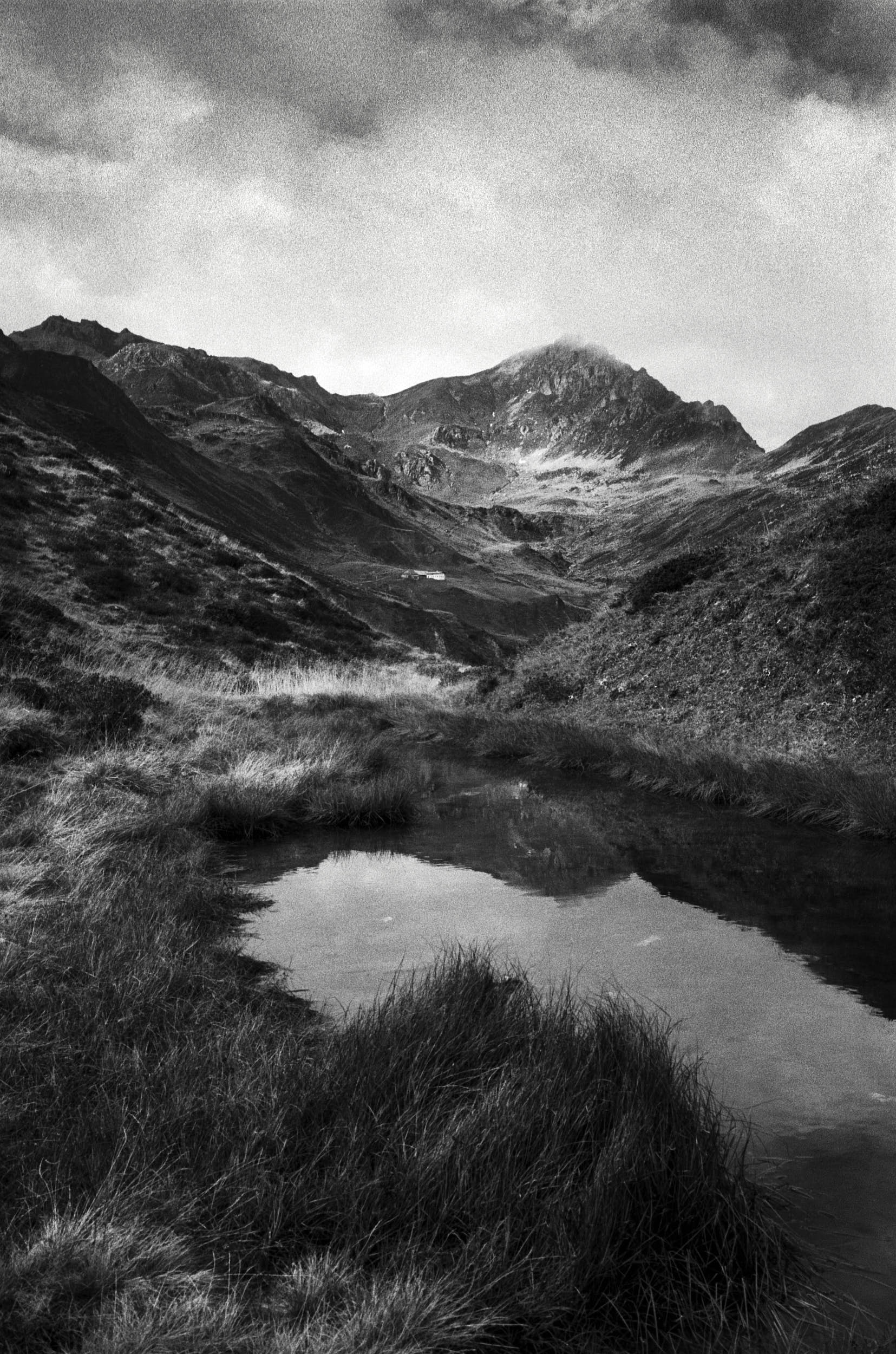 Beautiful mountain landscape with alpine peaks hiding in clouds and a pond in the foreground.