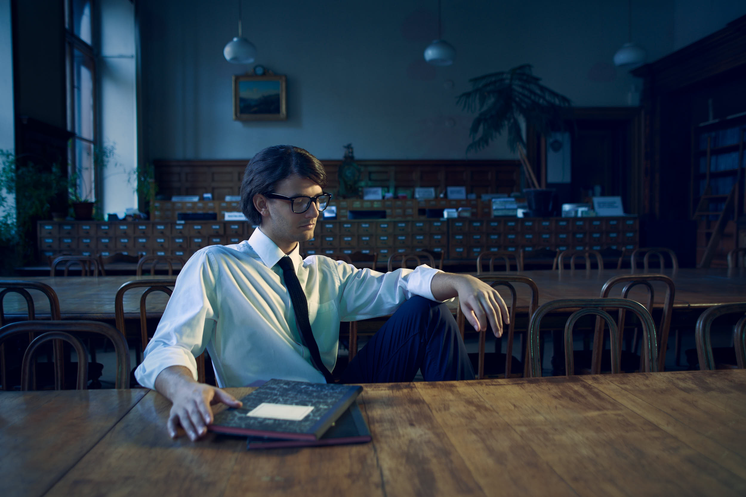 Student with glasses sitting in a library in a cinematic editorial photograph.