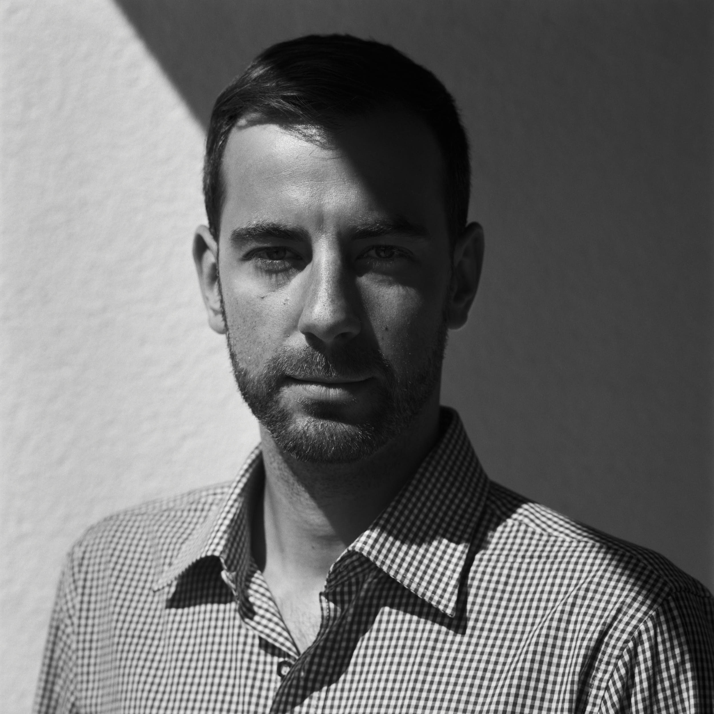 Contrasty portrait of a man with deep shadows wearing checkered shirt. Medium format film photography.