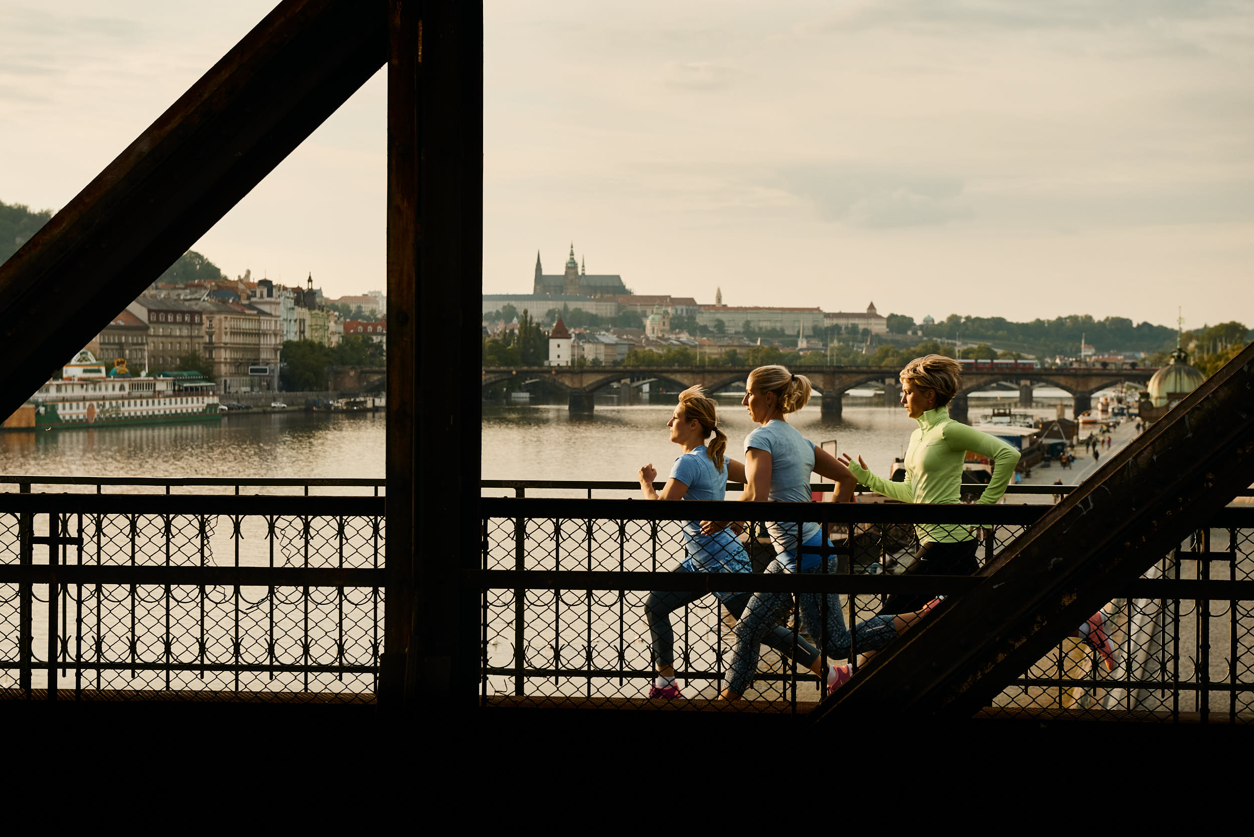 Group of women running across a railway bridge with Prague Castle in the background. Sport apparel advertising campaign.