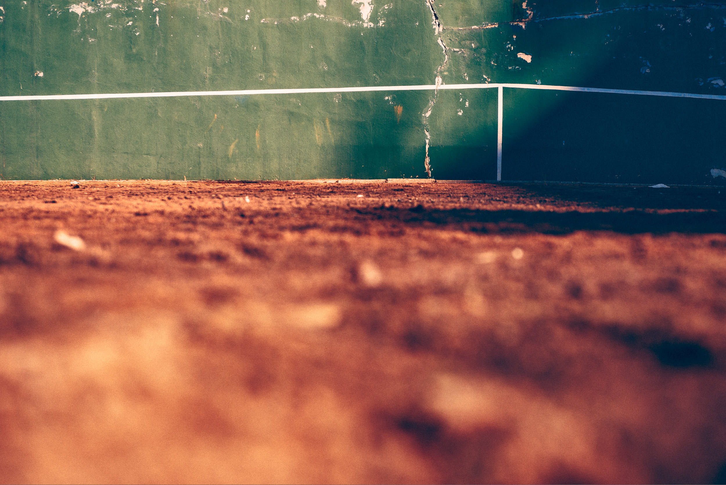 Minimalistic photography: green tennis practice wall with orange clay in the foreground.