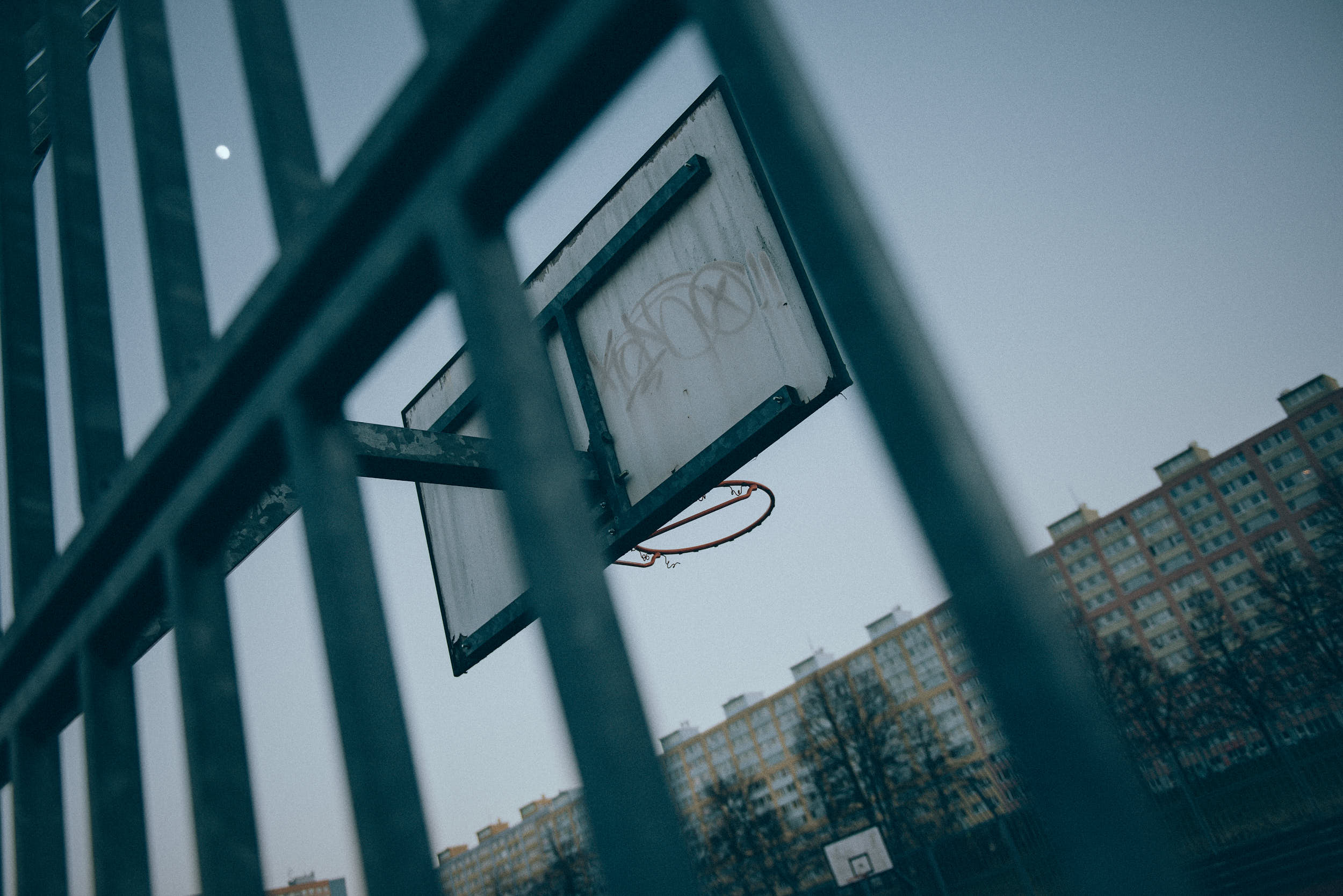 Trashed basketball hoop shot through metal fence.