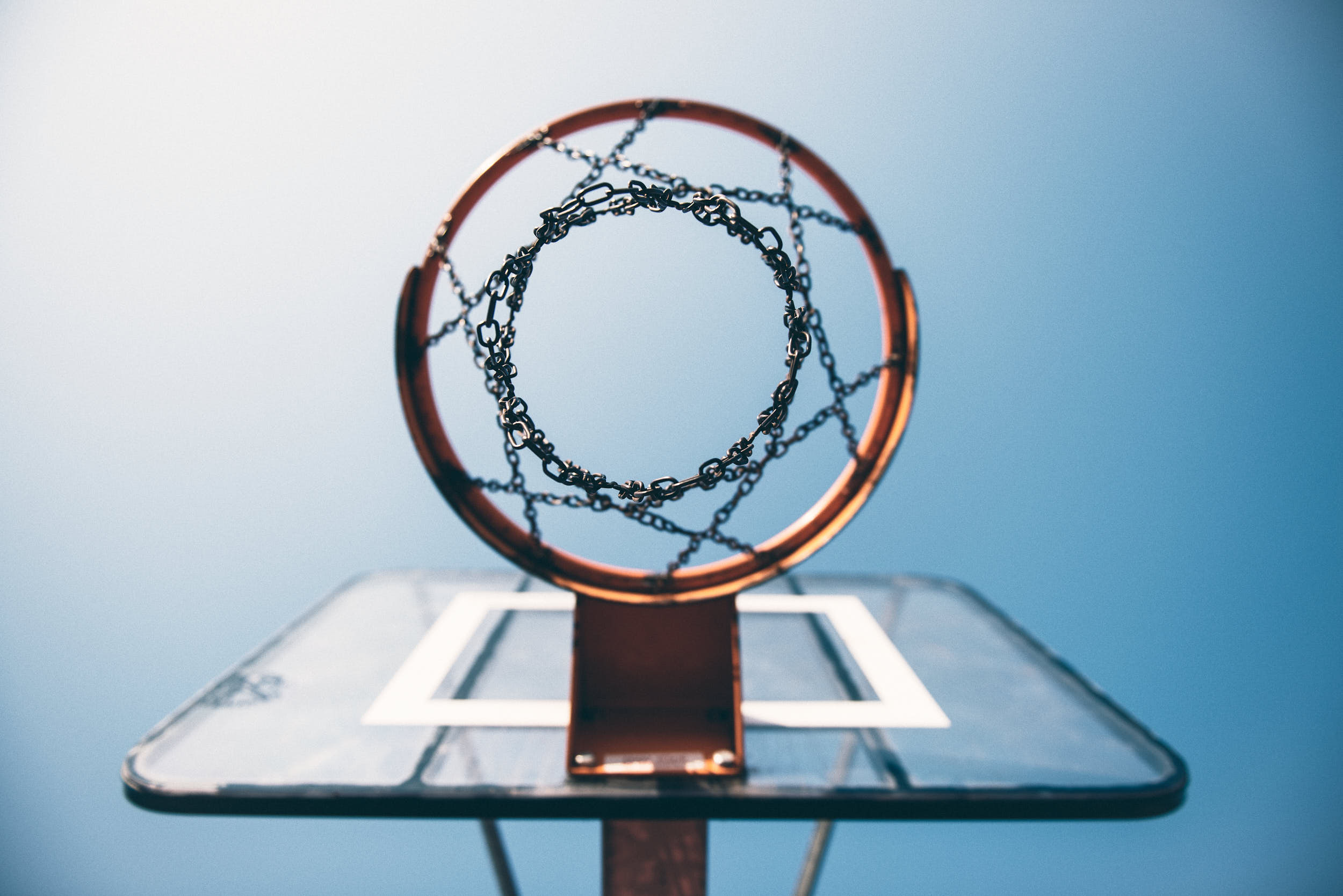 Basketball hoop with a chain net photographed from beneath with blue clear sky.