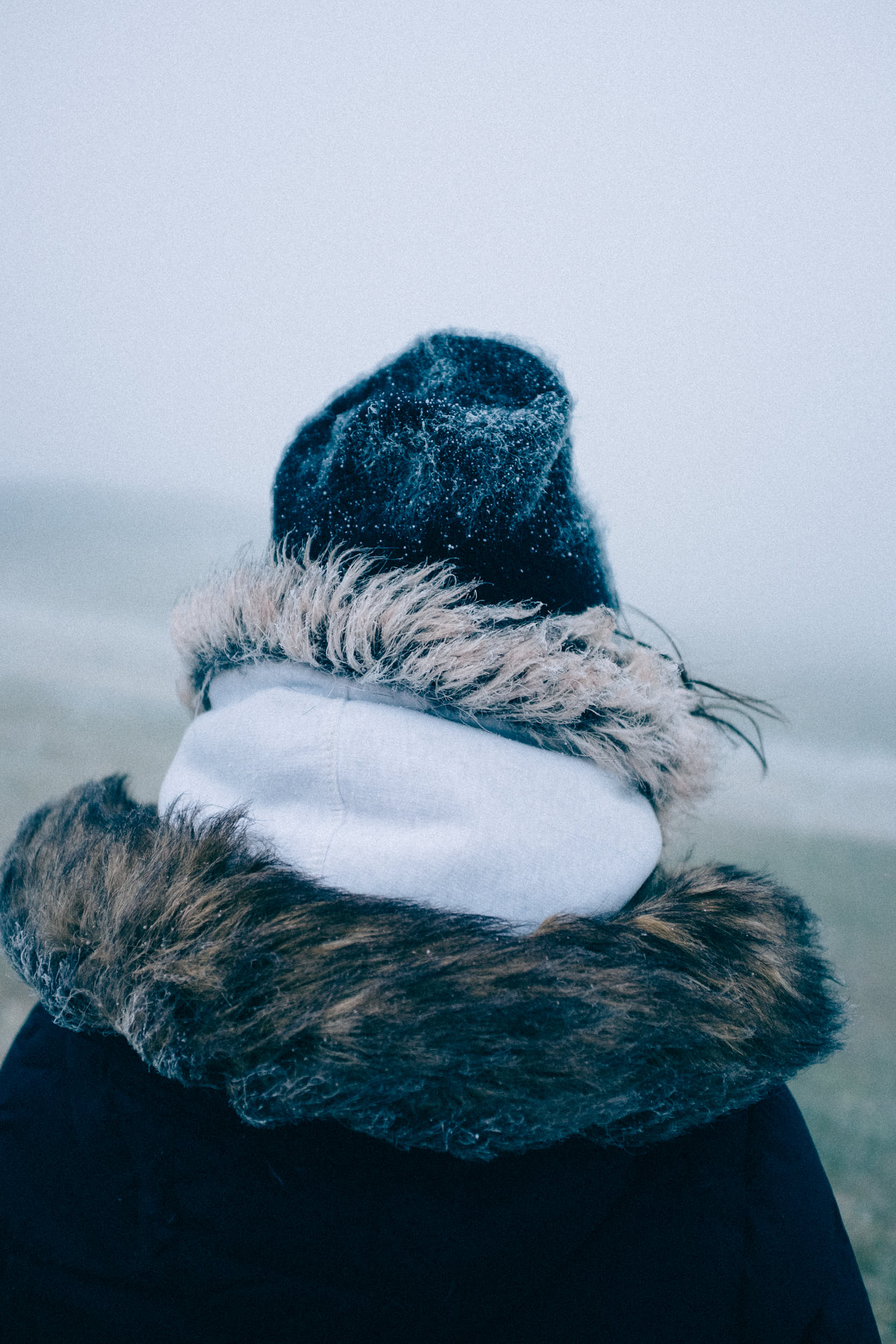 Woman standing on a mountain path with jacket and hat covered with ice.