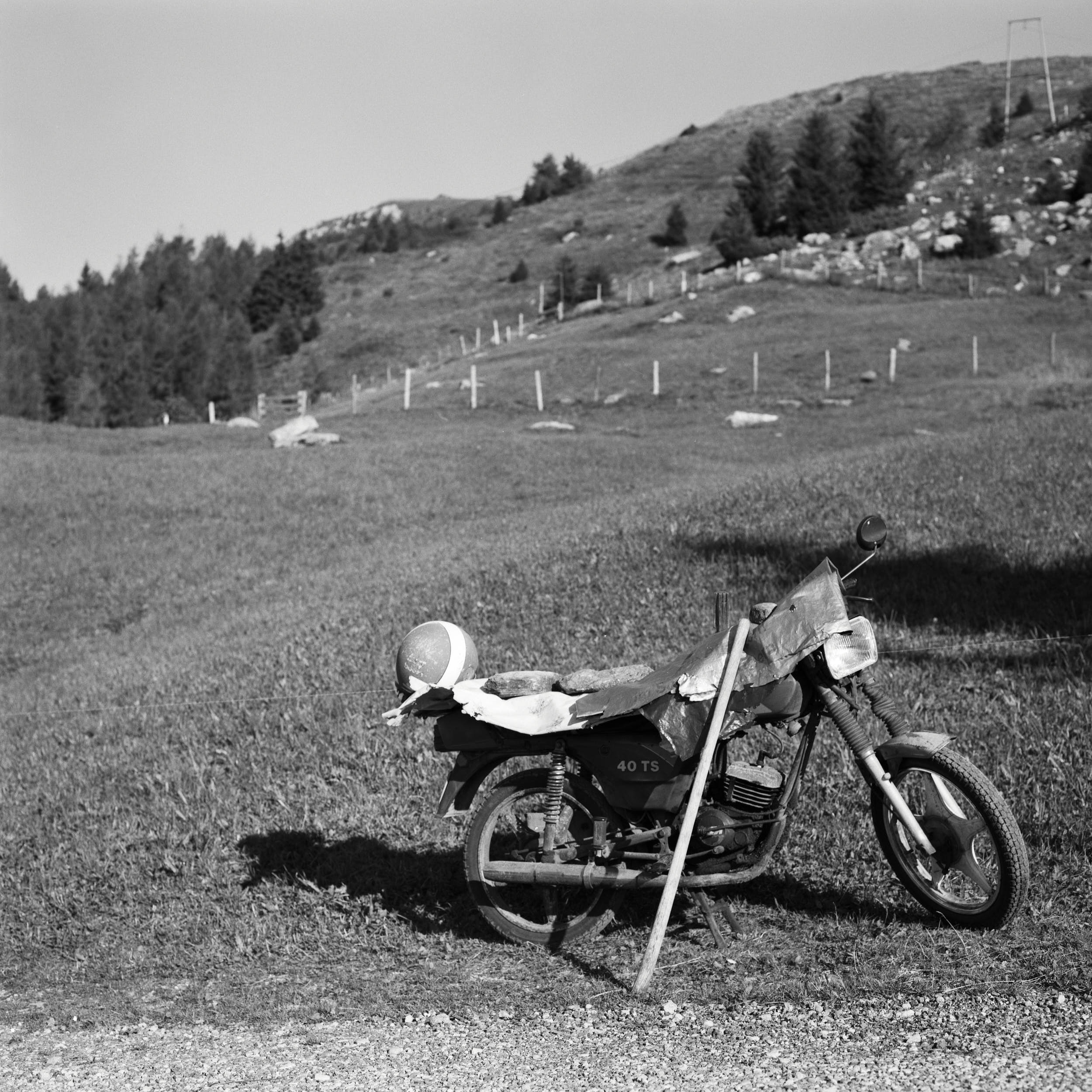 Black and white documentary photography: motorcycle parked on the side of a mountain road.