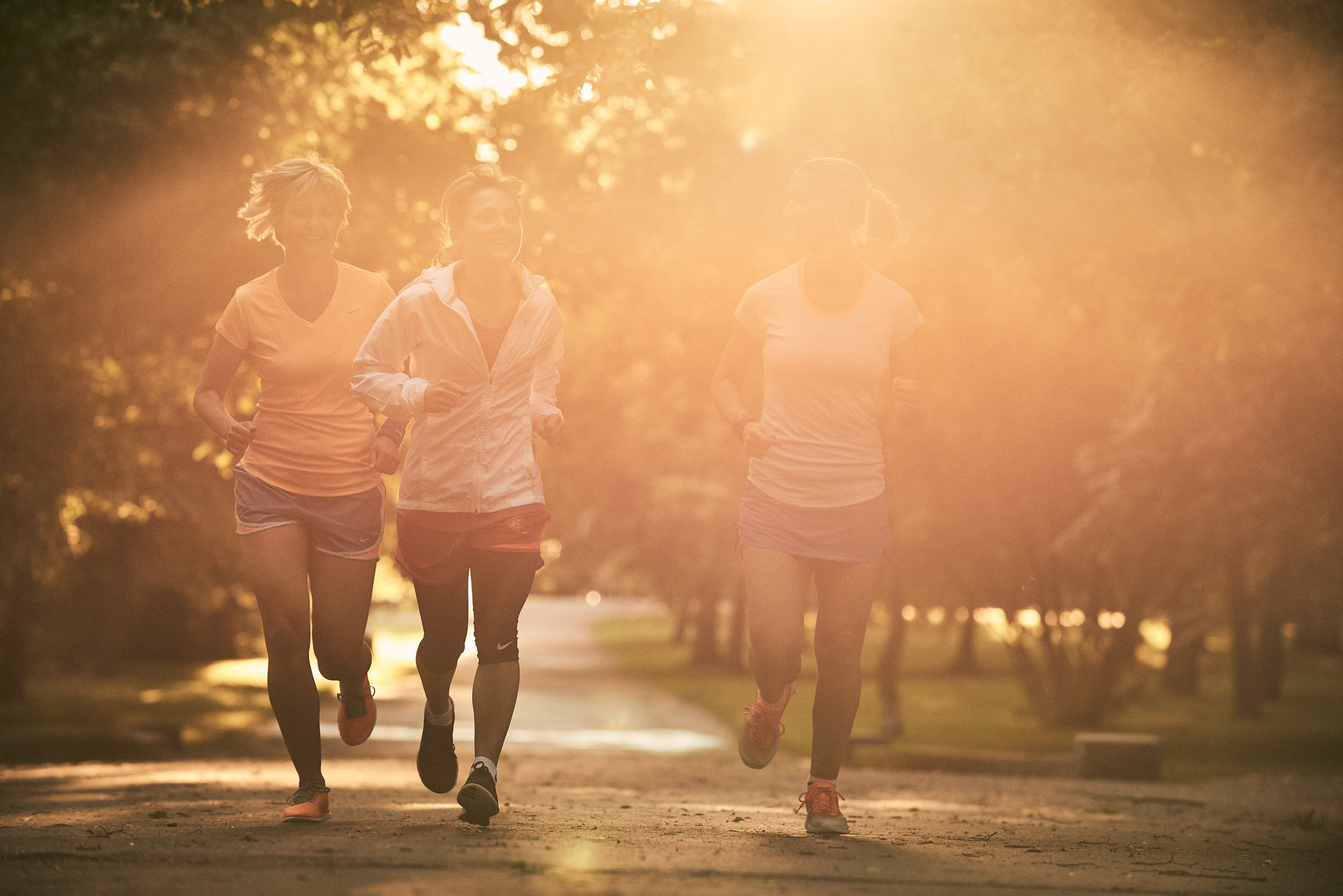 Group of girls running in a park with sunflare coming through the leaves.