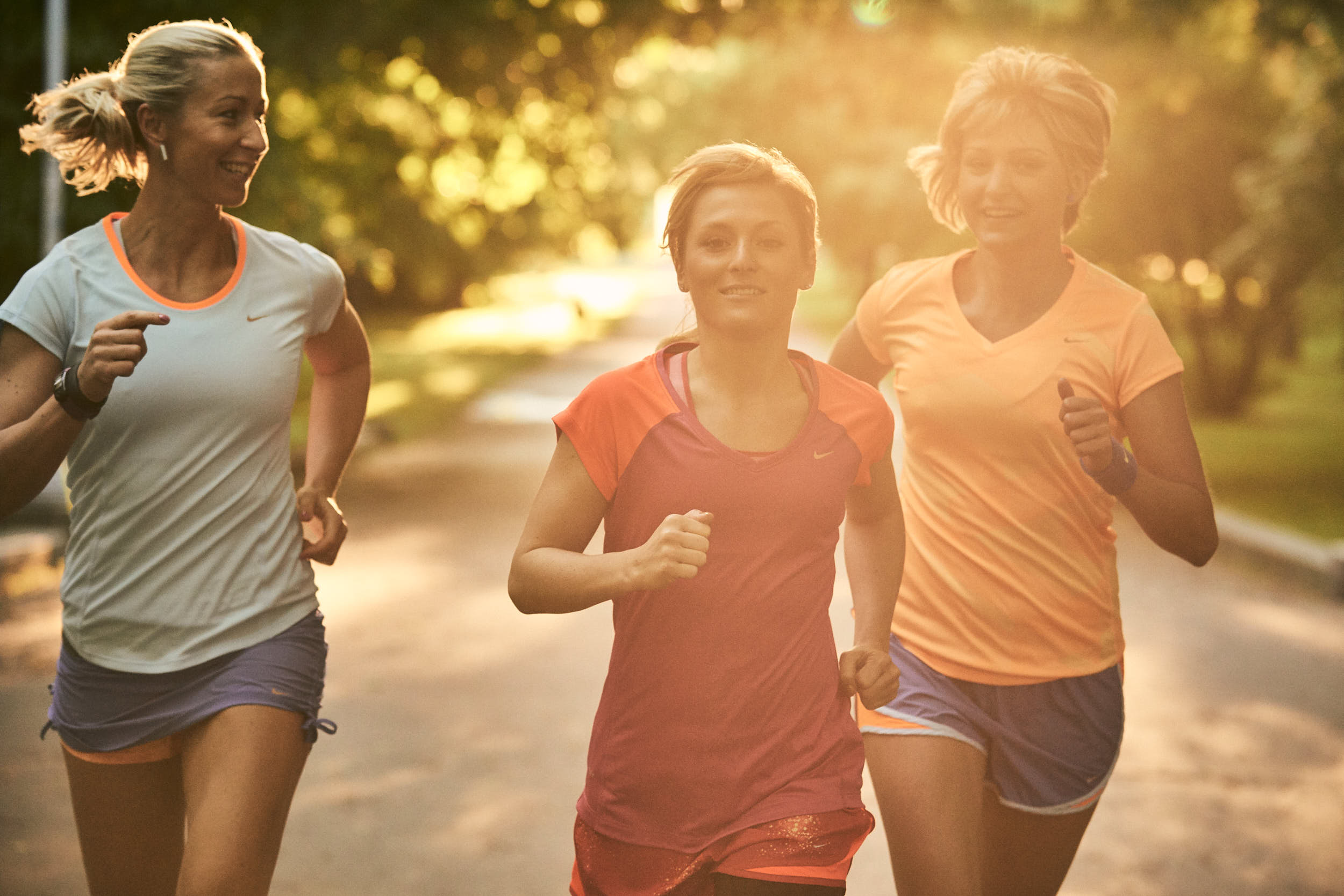 Group of girls running in a park with sunflare coming through the leaves.