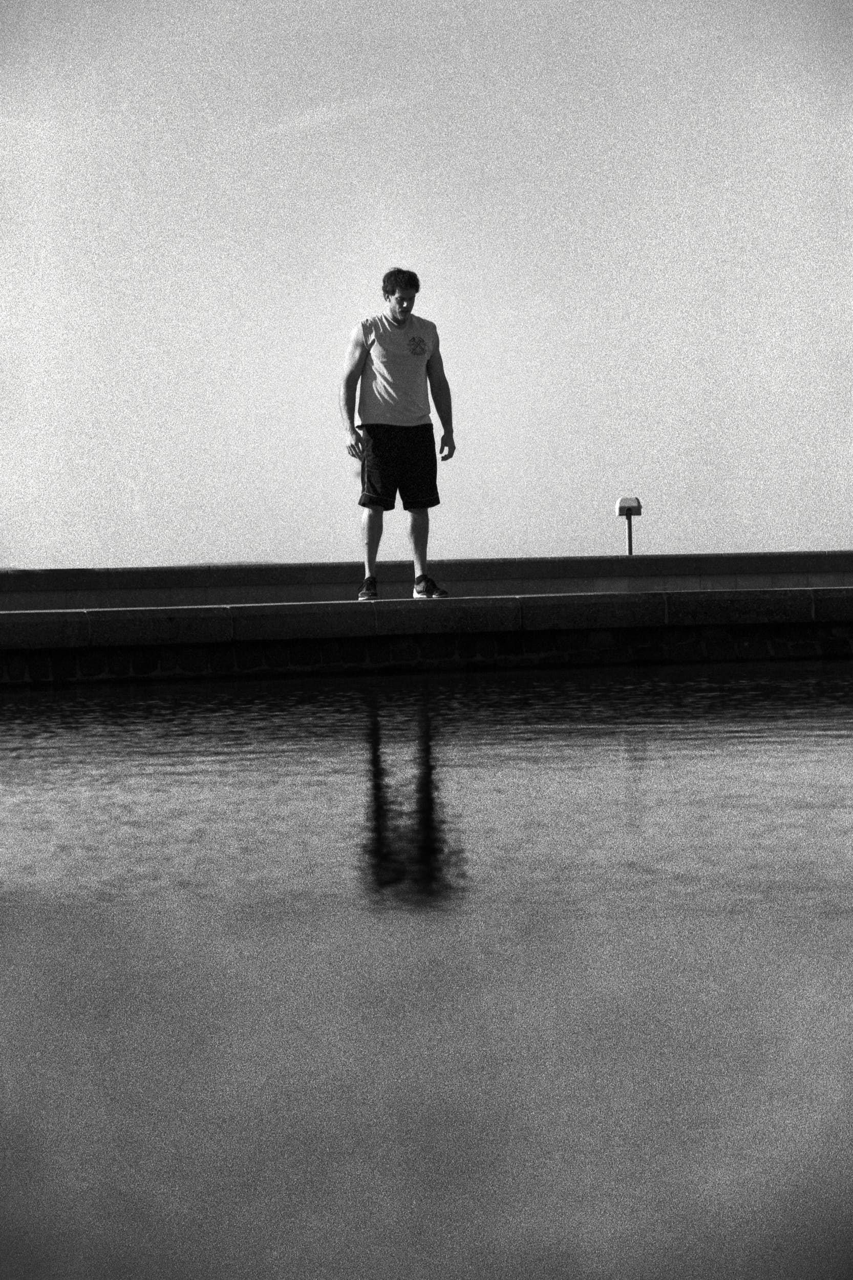 Fitness athlete standing on a curb. His body is reflected on a water surface beneath.