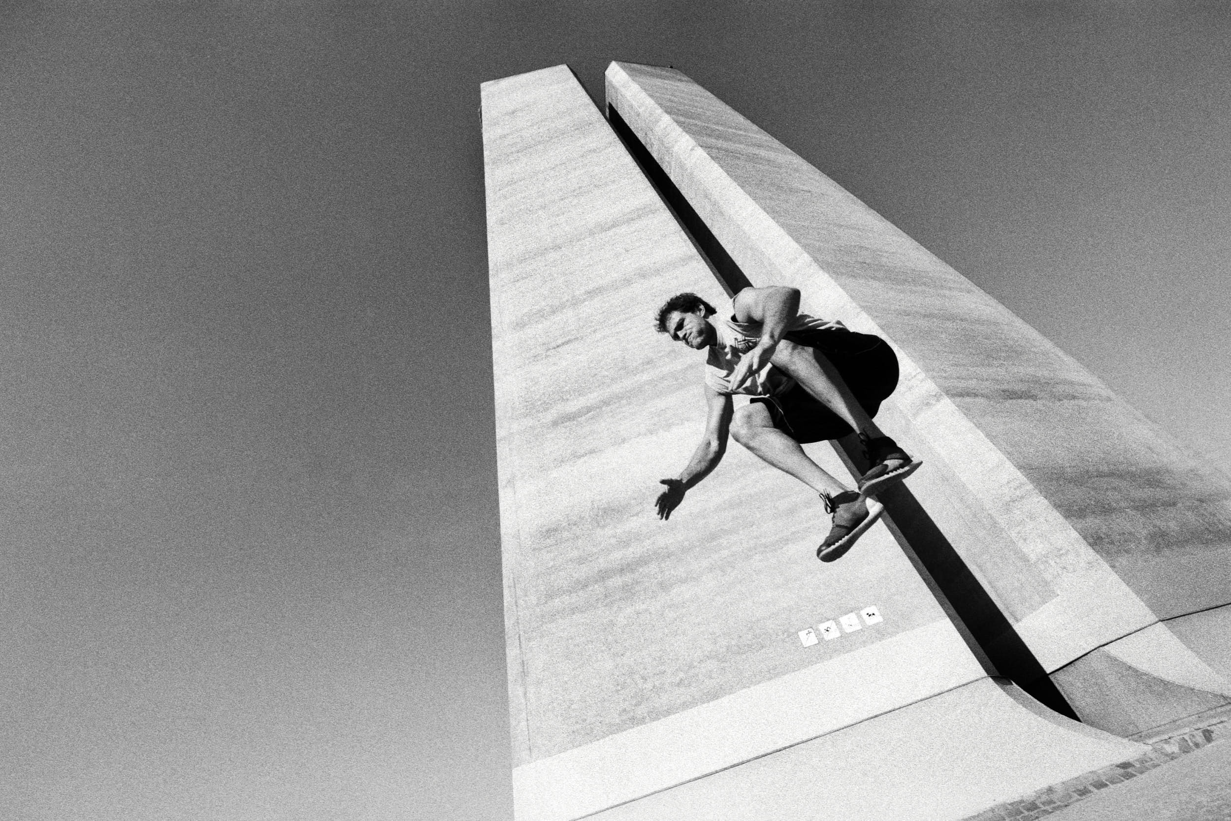 Fitness advertising photography: athlete jumping up with concrete brutalist structure in the background.